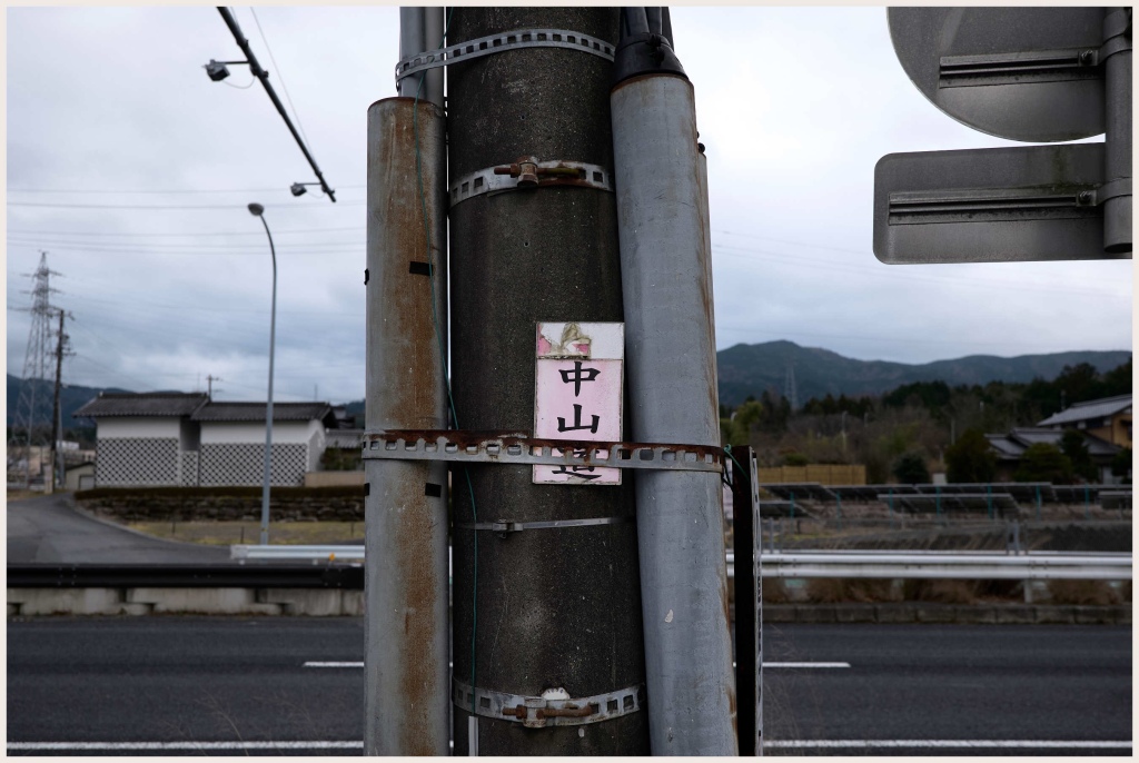An old pink Nakasendo sign attached to an electricity pylon on a cloudy, cold day.